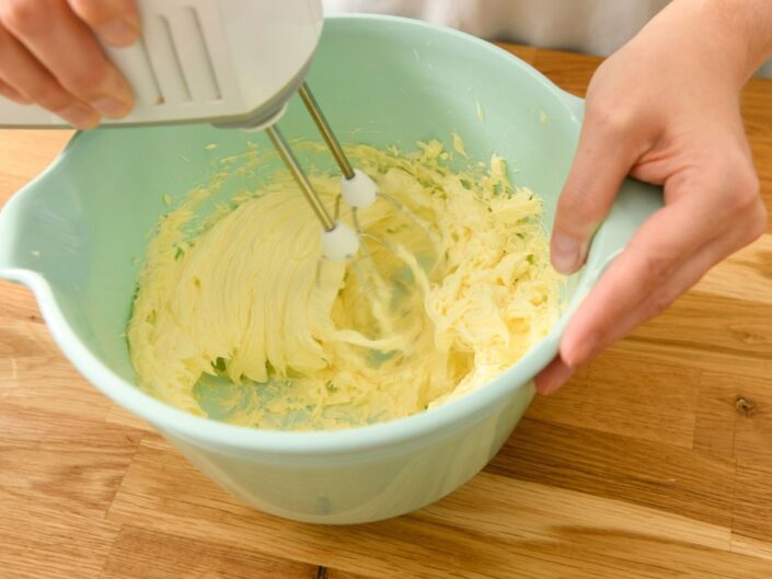 Nő robotgéppel krémet ver fel zöld kerámia keverőtálban