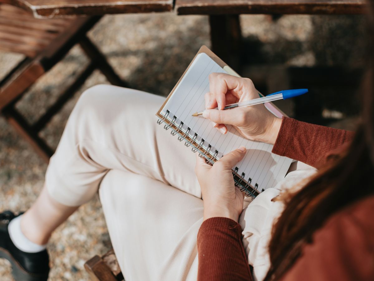 Nő kézzel ír jegyzetfüzetbe asztal mellett ülve