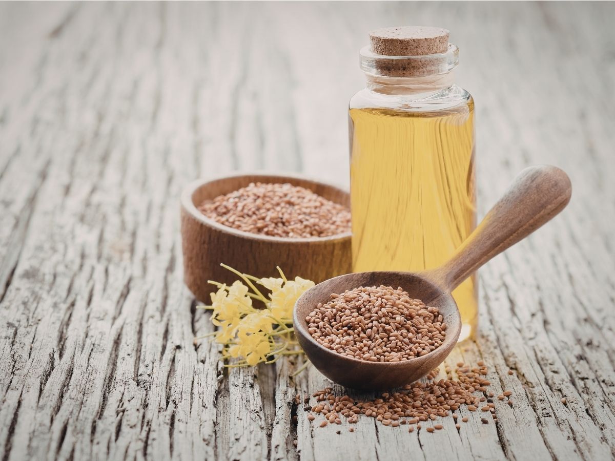 lenmag fa tálkában és kanálban mellette lenmagolaj üvegcsében