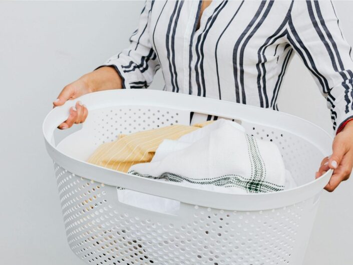 csíkos ruhás nő mosókosárral a kezében benne frissen kimosott ruhák