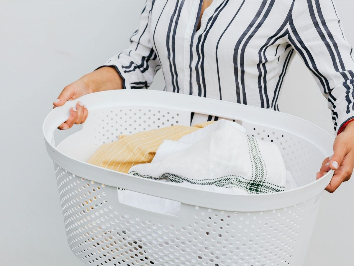 csíkos ruhás nő mosókosárral a kezében benne frissen kimosott ruhák