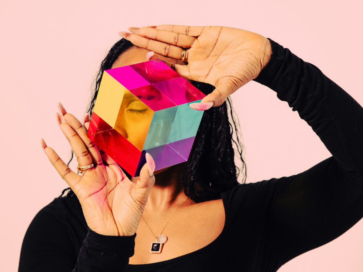 Számítógépes montázs fekete hajú nő, fekete felsőben színes prizmakockát tart az arca elé