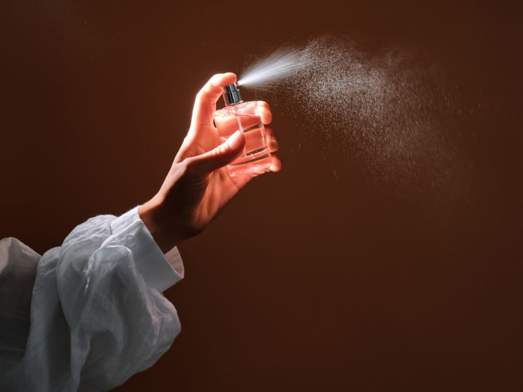 Nő buggyos ujjú blúzban illatosítót fúj ki az otthonában, sötét háttér