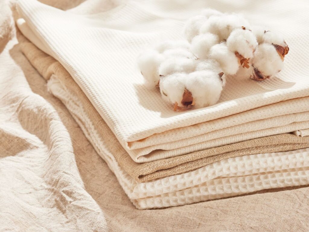 Pamut ágynemű neutrális színekben összehajtogatva ágyon, a tetején gyapot növény