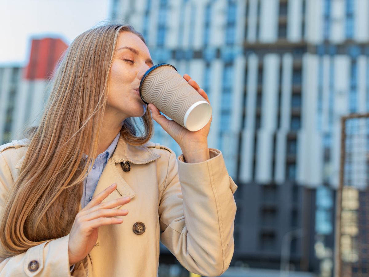 egy nő elvivős kávét iszik az utcán papírpohárból