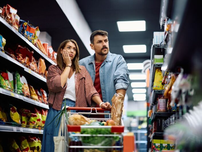 nő és férfi boltban bevásárlás közben sokkolva nézik az árakat