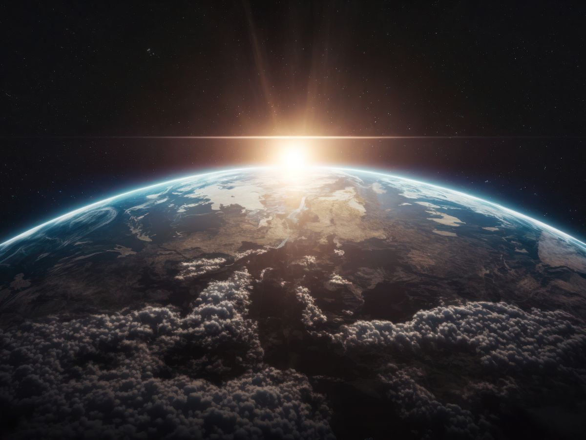 Napfelkelte a Föld pereme fölött az űrből nézve, ragyogó fény csillan a bolygó felszínén, felhőrétegek és a végtelen sötét világűr háttérben.
