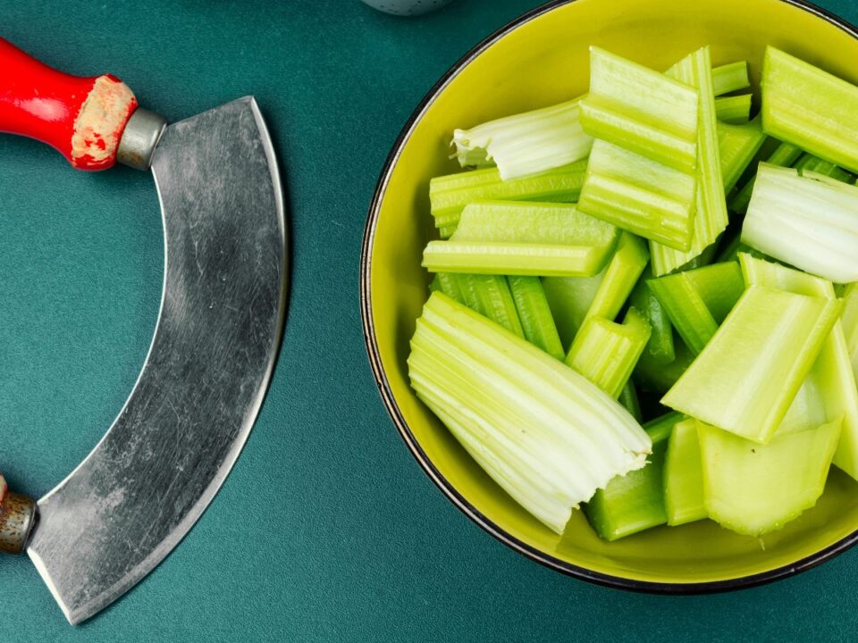 zero-kalorias-etel-mitosz - Nők Lapja Felülnézetből egy tál frissen felvágott zeller látható élénkzöld színben, mellette egy régi, ívelt pengéjű kés. Letisztult, egyszerű kompozíció, amely a „negatív kalóriás” étel mítoszát idézi.