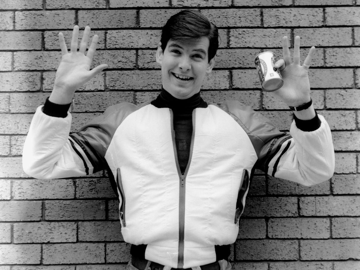 Pierce Brosnan 1978-ban téglafal előtt áll Írországban, felemeli a kezét, egyik kezében sörösdoboz