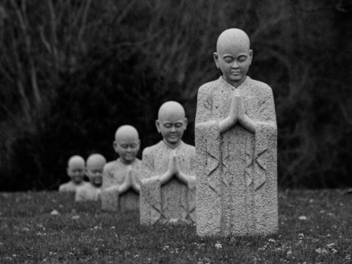 Szürke hangulatú képen 5 Buddha szobor egymás mögött, egyre alacsonyabbak és közelebb a földhöz