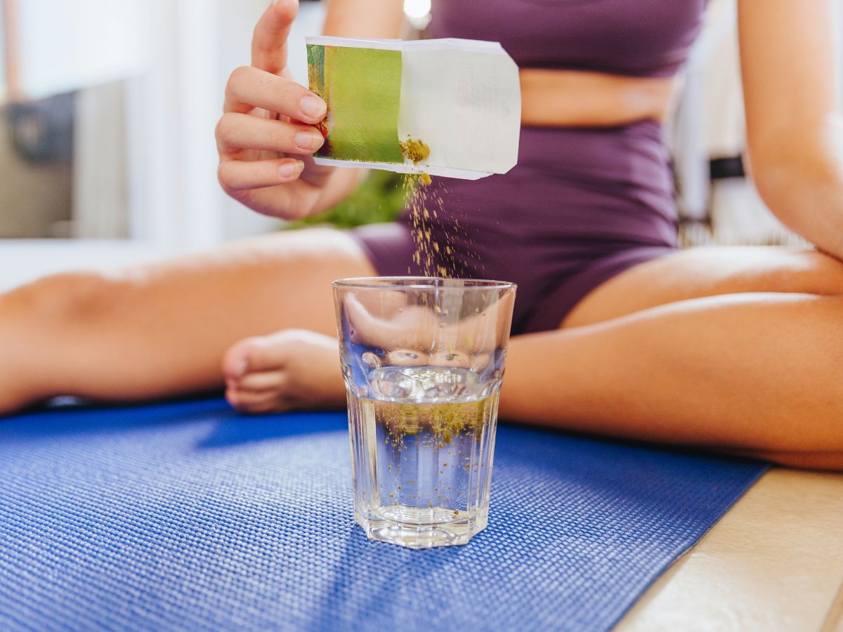 Nő fitness ruhában kék matracon ülve pohár vízbe chia őrleményt szór