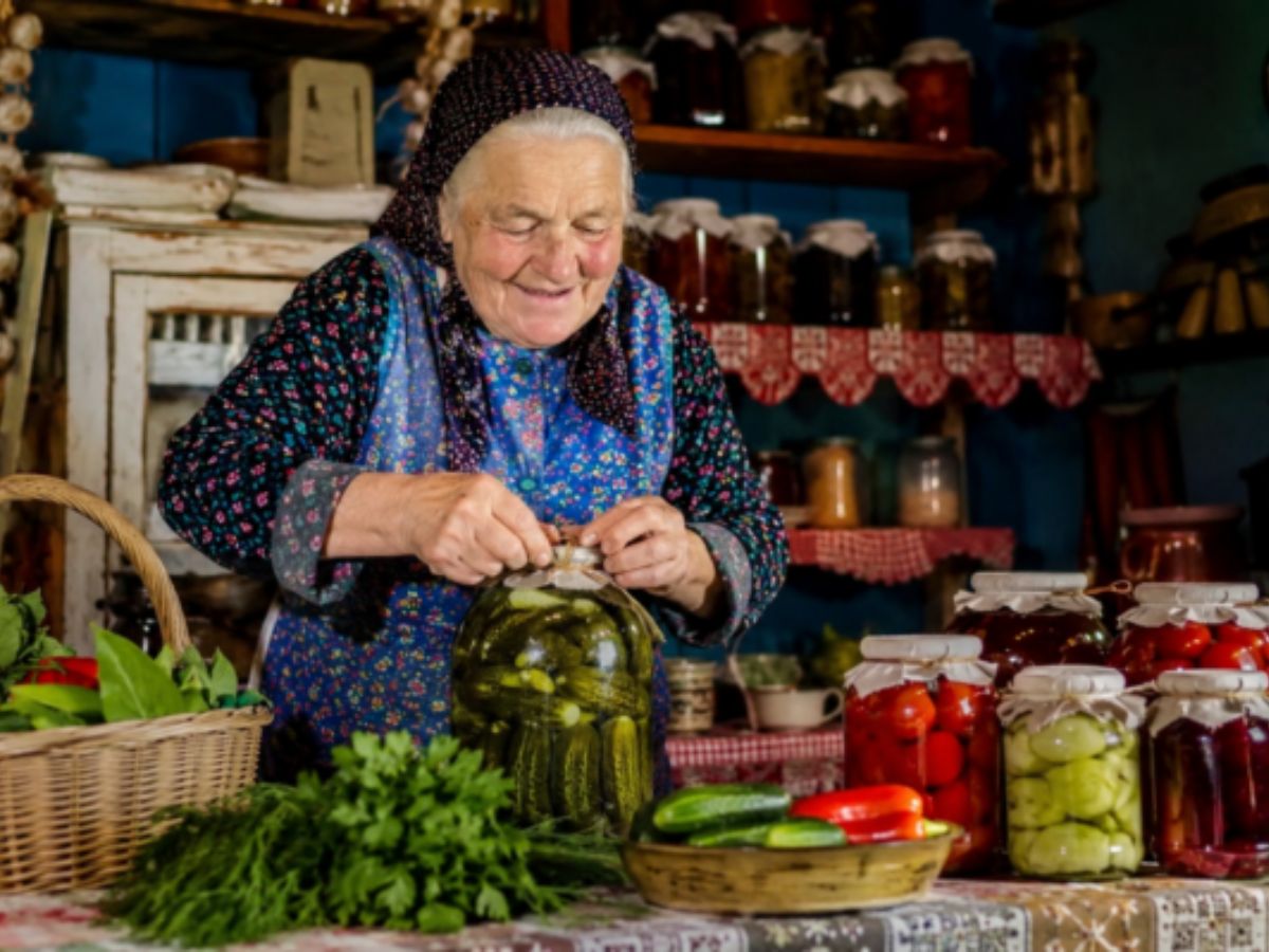 idős fejkendős nő kovászos uborkát tesz el a konyhában
