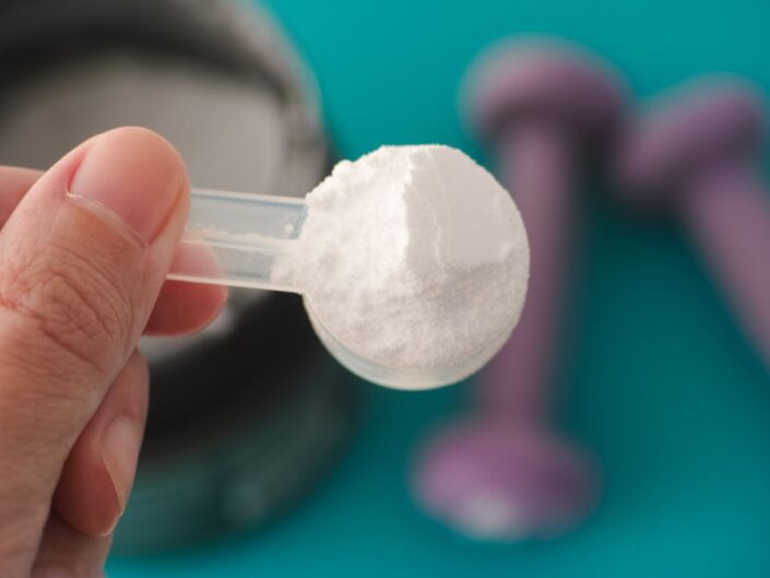 glutaminpor mérőkanálban alatta egy pár kézisúlyzó