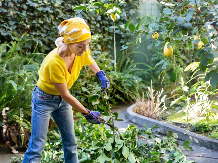 Csinos nő sárga pólóban és farmerben, kendővel a fején kertészkedik