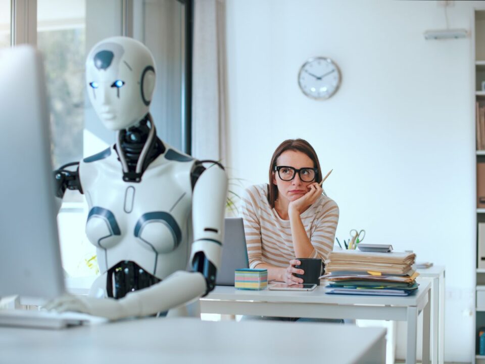 mesterseges-intelligencia-noi-munkak - Nők Lapja frusztrált nő ül az irodában és nézi az előtte ülő női robotot