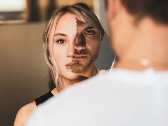 Szőke, fiatal nő rémült arccal néz, arca egy részét borostás, fekete szemű férfi kitakarja tükörrel, a férfi erőszakos, elszánt nárcisztikus tekintettel néz