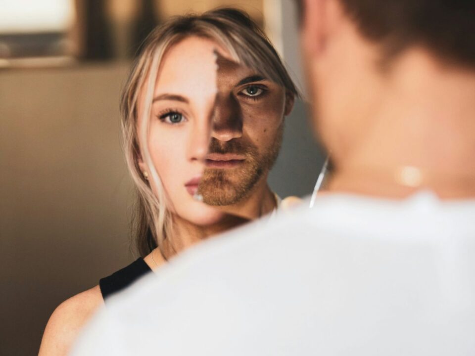 narcisztikus-osszeomlas - Nők Lapja Szőke, fiatal nő rémült arccal néz, arca egy részét borostás, fekete szemű férfi kitakarja tükörrel, a férfi erőszakos, elszánt nárcisztikus tekintettel néz