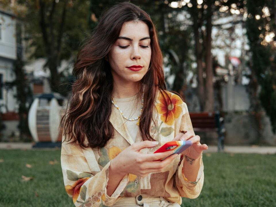 Szép fiatal barna hajú nő szöveges üzenetet küld a telefonján a parkban