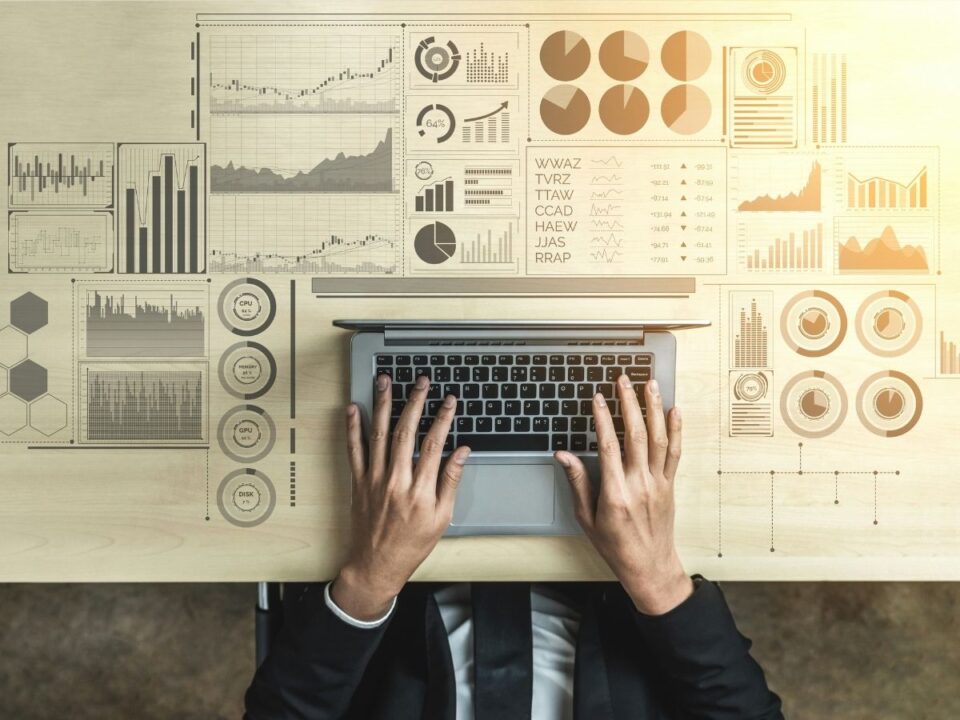adatelemzo-legunalmasabb-munka - Nők Lapja Adatelemző munka közben felülnézetben, laptopon gépel, körülötte grafikonok és diagrammok adatokkal