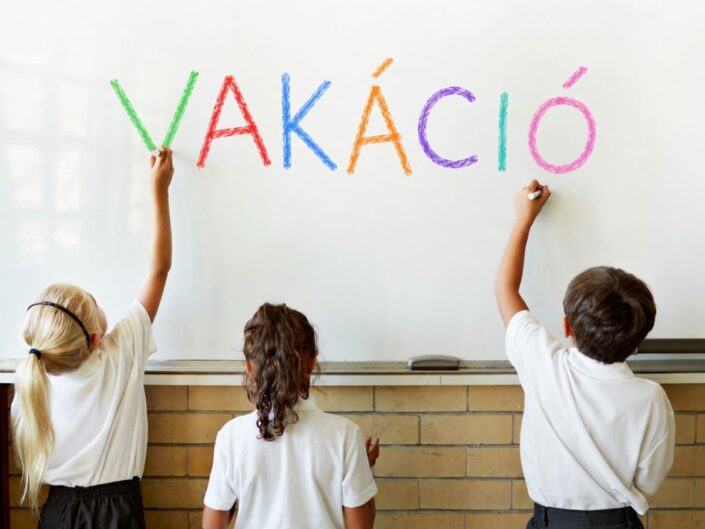 Három gyerek háttal a kamerának a vakáció feliratot írja fel fehér táblára