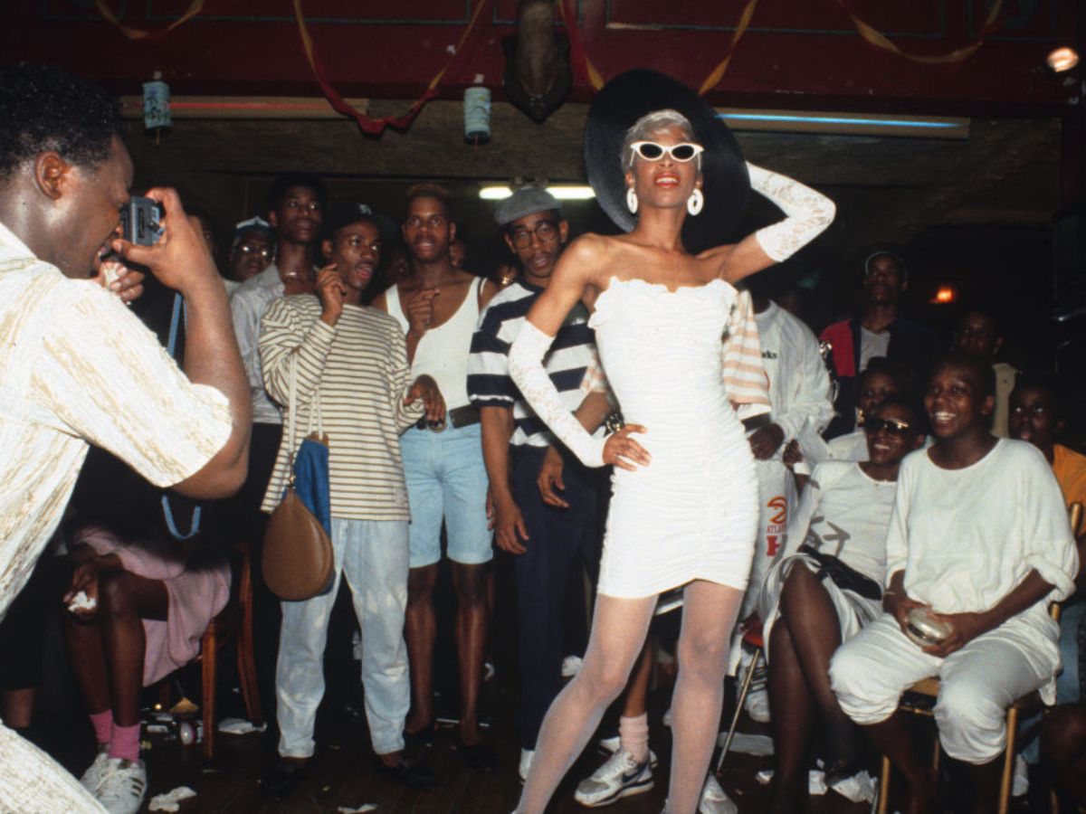 Octavia St. Laurent drag queen 1988-ban a harlemi drag bálon – fiatal fekete férfiak állnak és ülnek mögötte (az arcukat látjuk), mosolyognak, nevetnek, miközben egy másik férfi fotózza Octaviát.