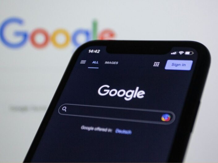 Google keresés fekete telefon kijelzőjén, háttérben elhomályosítva Google színes logó