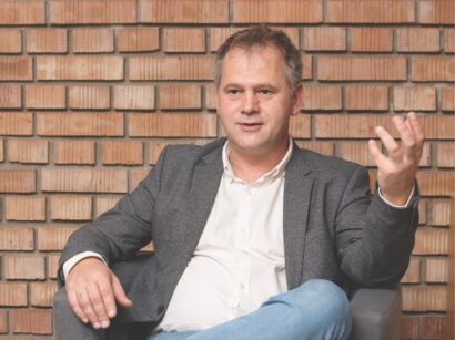 Kendeh-Kirchknopf Péter evangélikus lelkész ül egy téglafal előtt, beszéd közben készült róla a kép