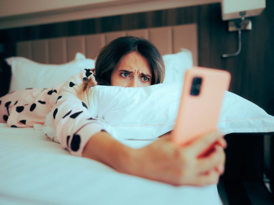 Aggódó nő ágyban fekve nézi a telefonját – stock fotó