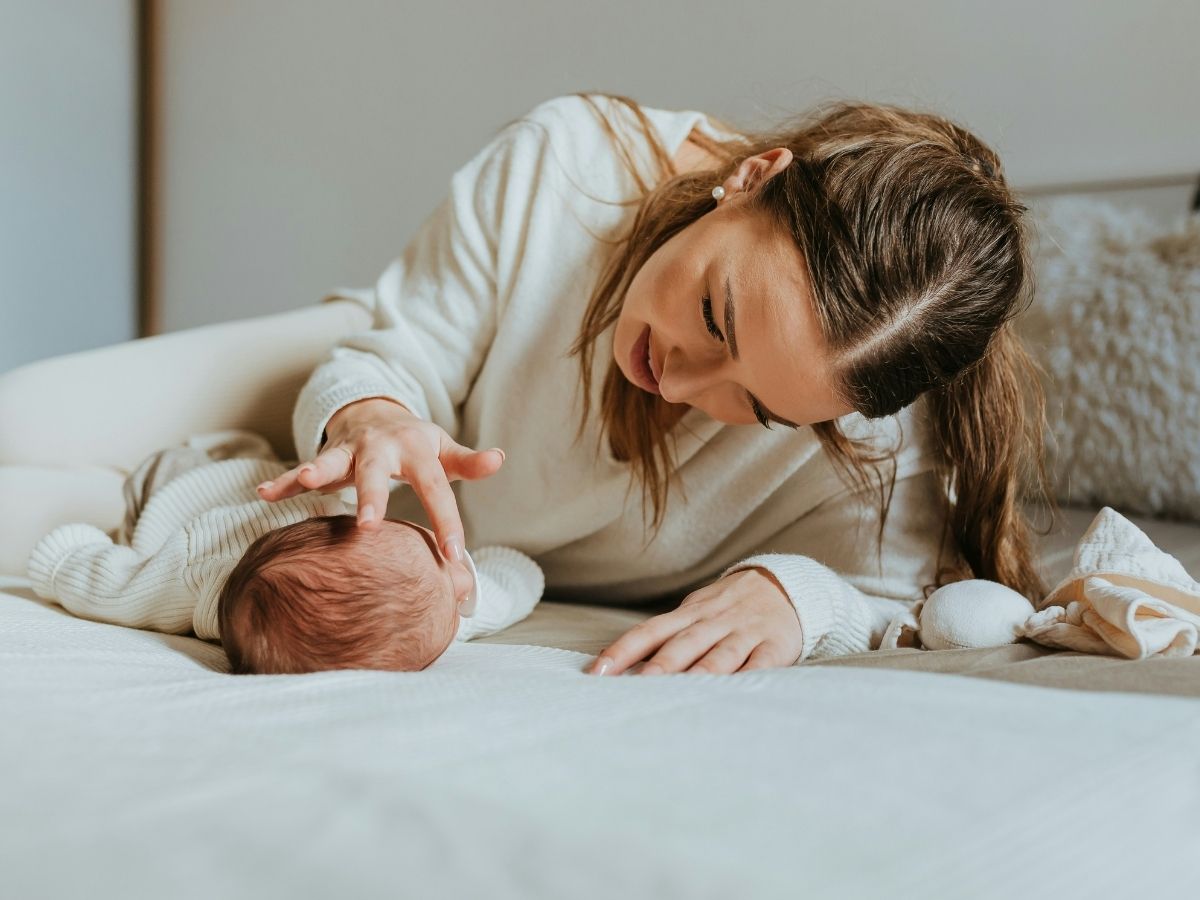 Anya és újszülött gyermeke natúr színvilágú képen ágyon fekve