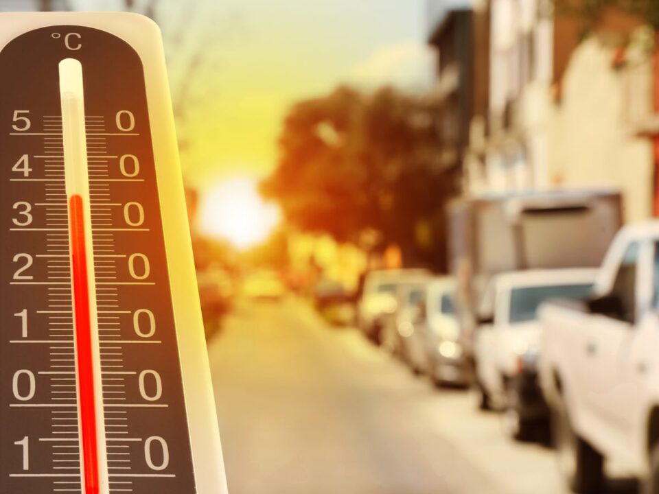 A háttérben forró nyári utcát vakító napsütés borít, az előtérben álló kültéri hőmérő higanyszála 30 °C fölötti hőmérsékletet mutat, érzékeltetve a hőség intenzitását.