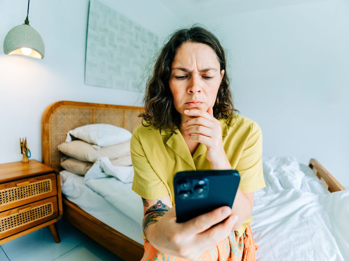 Stresszes nő okostelefonnal a hálószobában