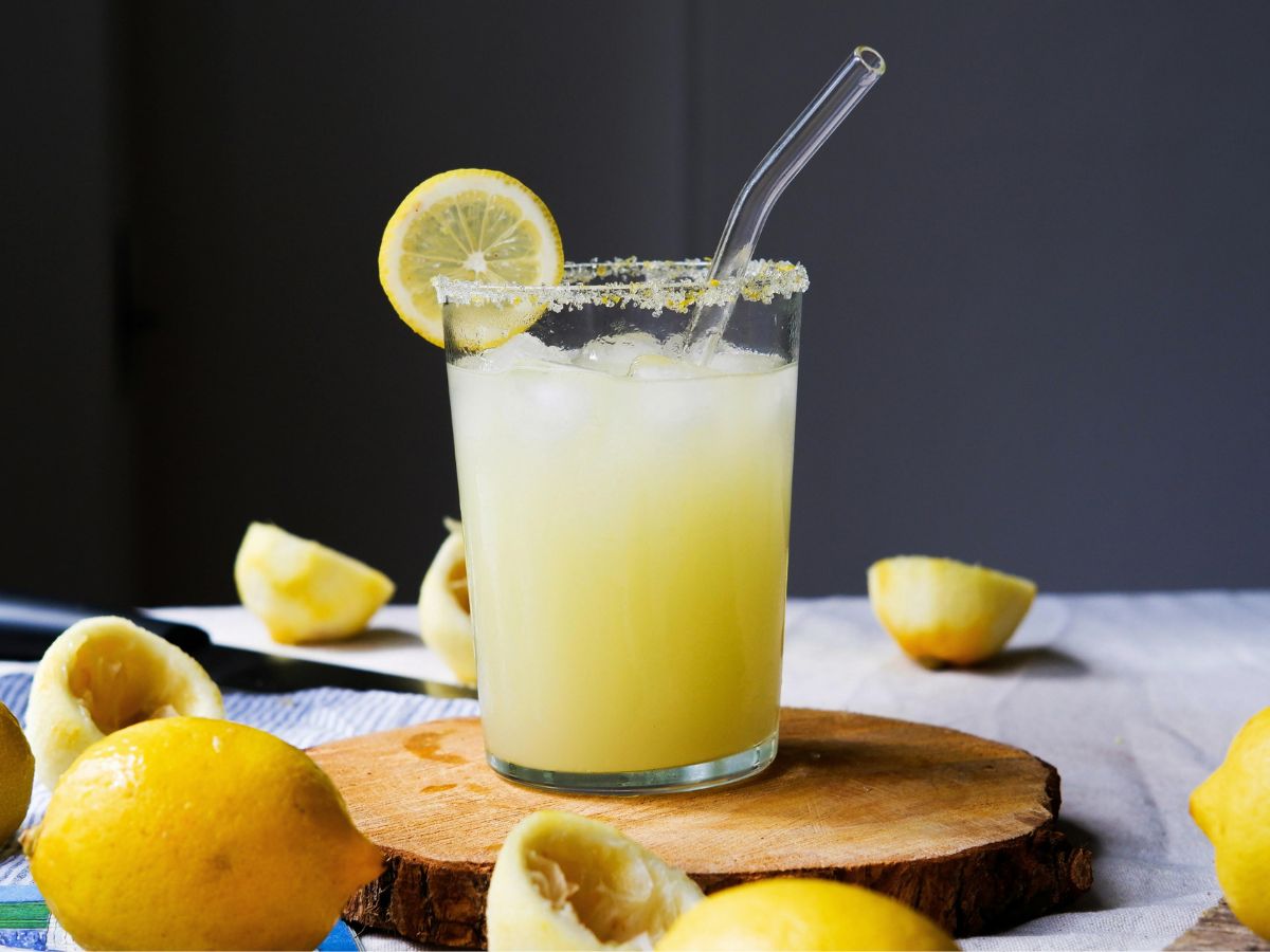 sötét háttér előtt egy pohár jeges török limonádé egy kis fa tálcán, körülötte citromok