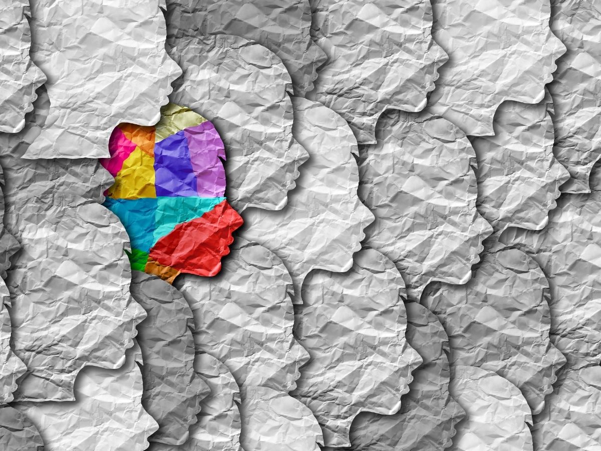 Gyűrött papírból készült illusztráció, szürke, egyforma emberfej profilok, egyetlen színes középen az autizmus spektrumzavart szimbolizálja
