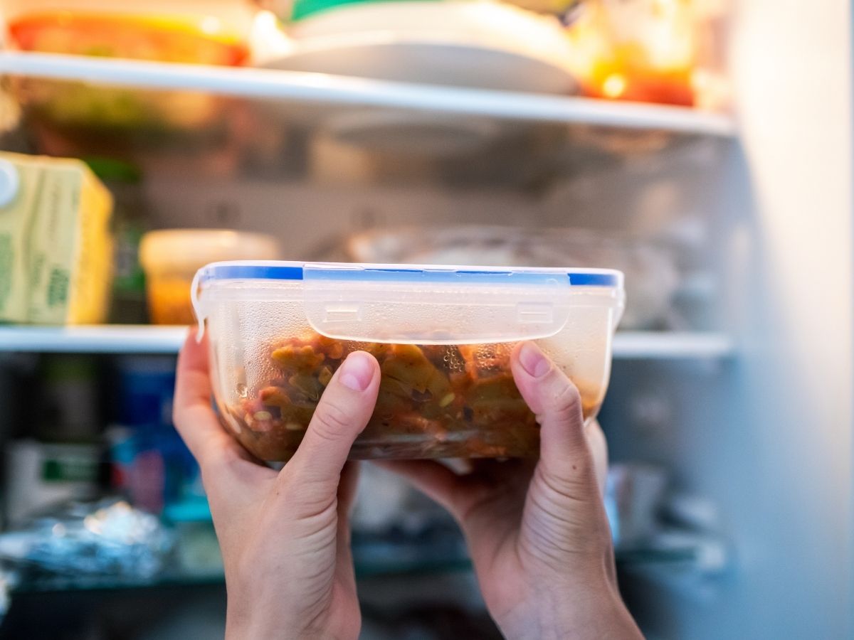 Női kéz műanyag tárolóedényben piros ételt vesz ki a hűtőszekrényből