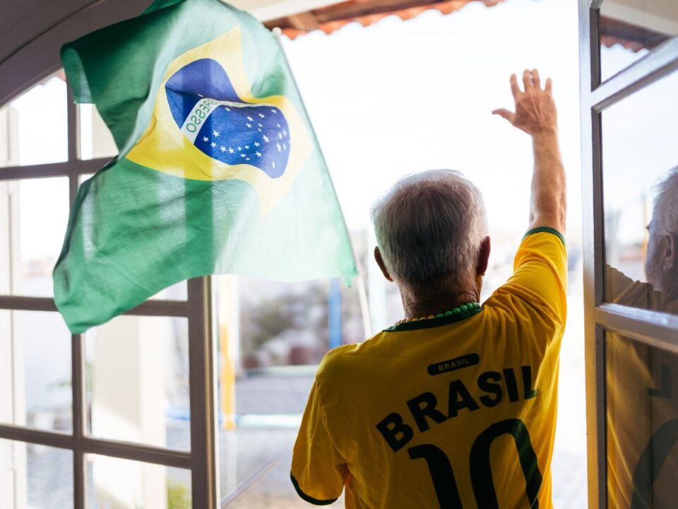 idosek-ablaknal - Nők Lapja Brazil válogatott mezét viselő idős férfi áll a nyitott ablaknál, integet az utcára, mellette brazil zászló lobog.