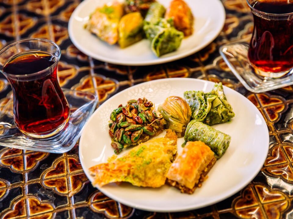 egy csempés asztalon két török teás pohár és két tányér, amin török édességek (például baklava) van