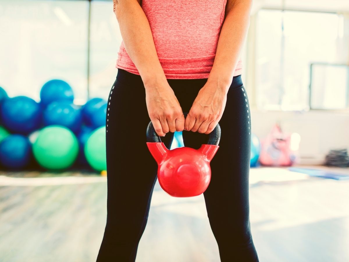 50 feletti nő törzse rózsaszín felsőben, fekete leggignszben piros kettlebellt tart a kezében