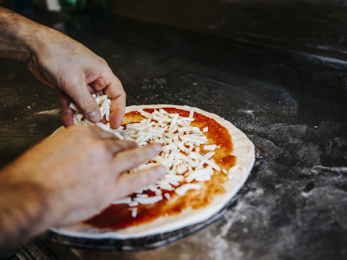 reszelt sajtot szórnak pizzára