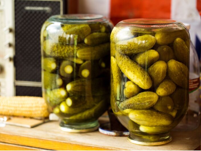 Két fejjel lefelé fordított befőttesüveg áll egy konyhapulton, bennük különböző méretű, egész uborkák sárgászöld lében.