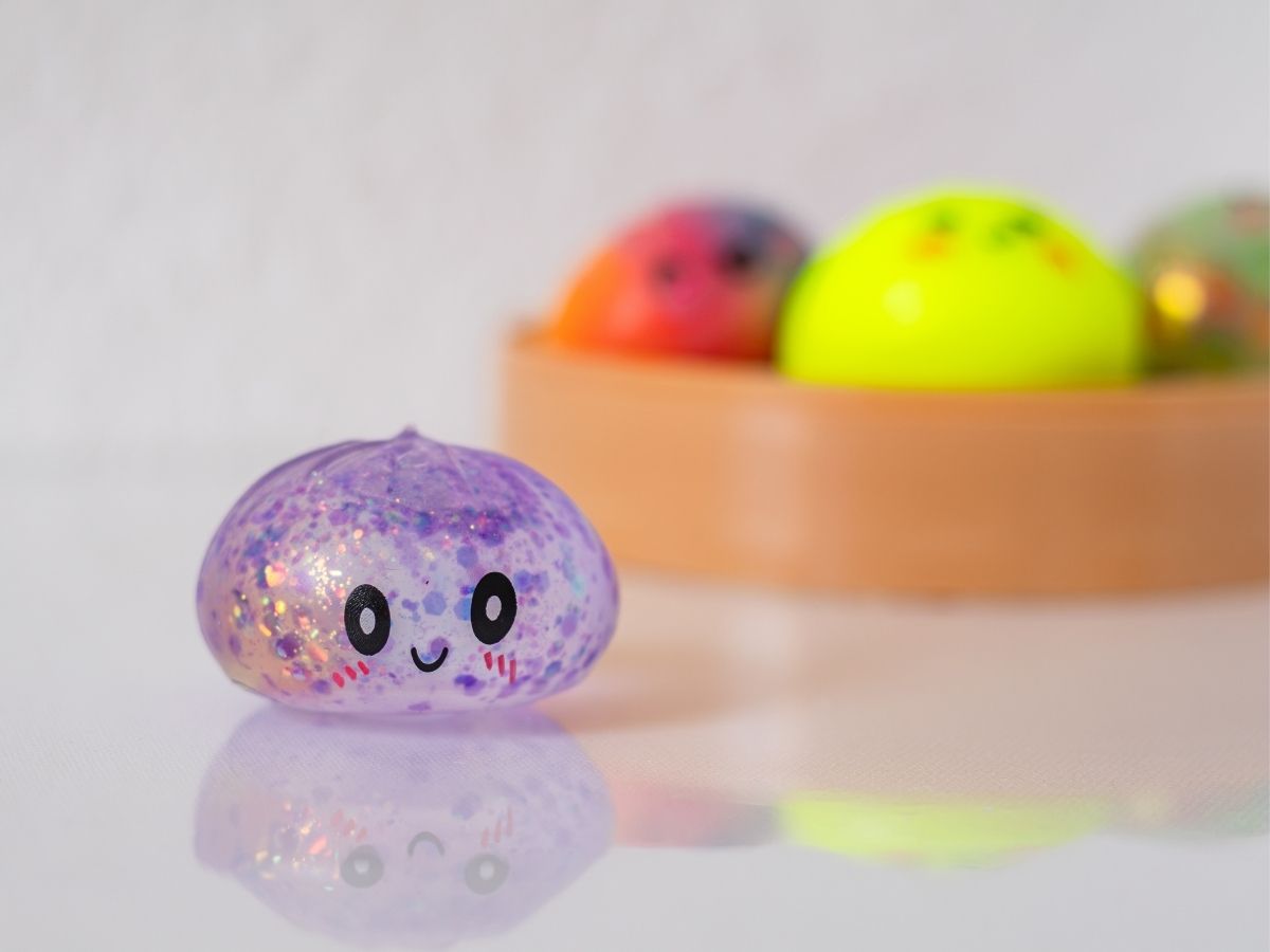 Lila glitteres squshy dumpling szenzoros játék, háttérben kosárban még több színes gombóc