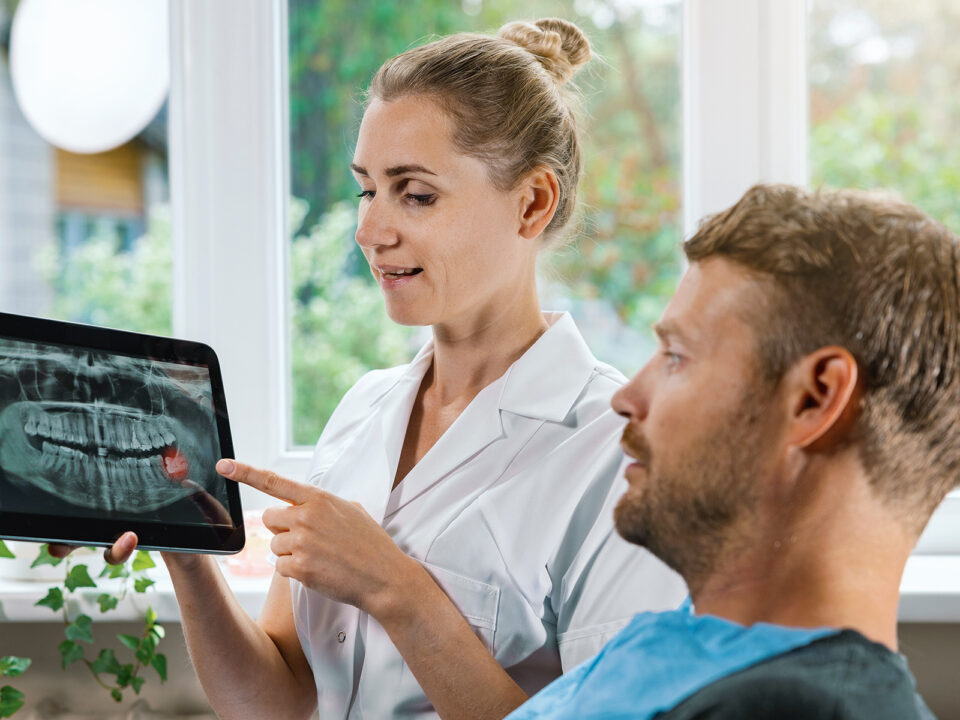 dentist showing and explaining dental x-ray picture with impacted wisdom tooth to his patient - Nők Lapja