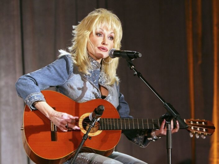 Dolly Parton farmerruhában, gitárral a kezében énekel 2006-ban
