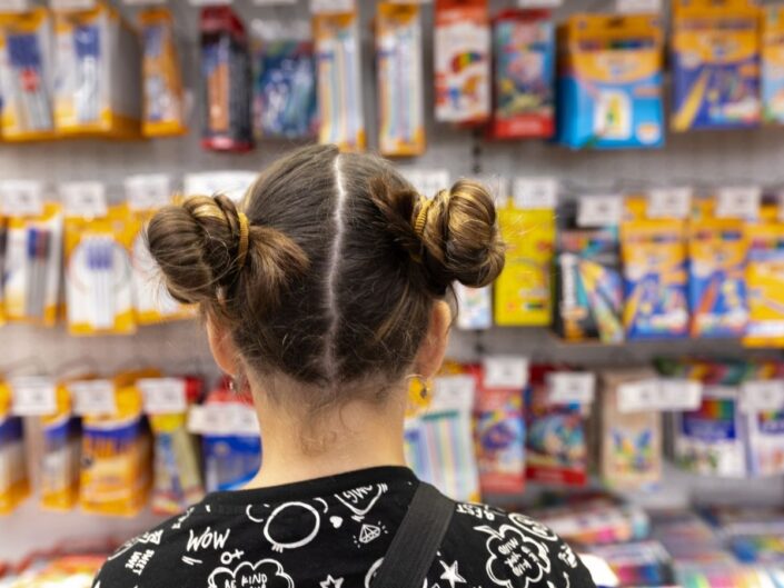 kislány háttal az iskolai eszközöket tartalmazó polcok előtt