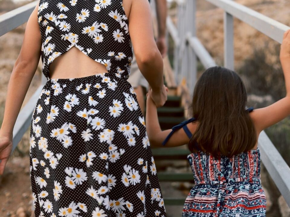 Anya fekete alapon fehér margarétás ruhában kislányával, háttal a kamerának lépcsőn mennek fel