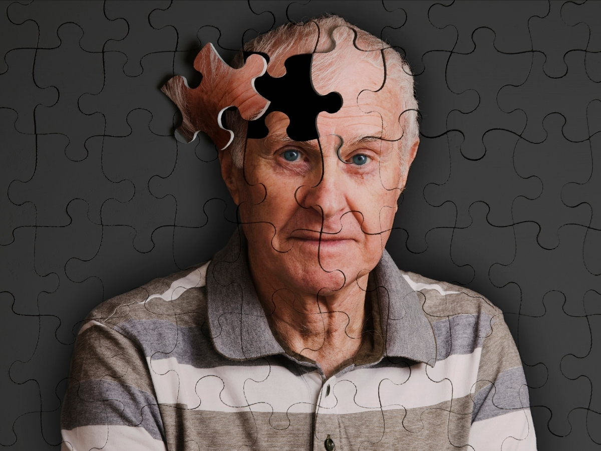 Idős férfi szürke háttér előtt, puzzle vonalakkal, fejének egyik része elmozdítva a kirakósban