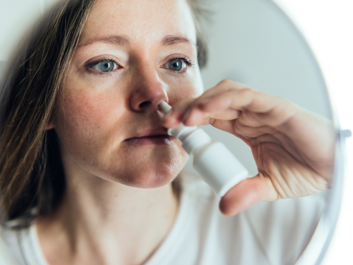 Nő tükör előtt állva orrspray-t fúj az orrába