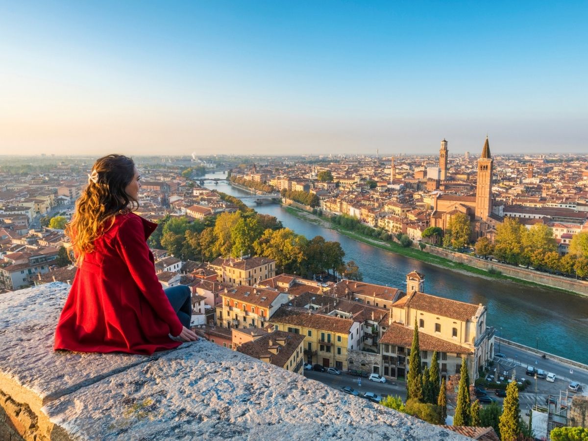 Vörös kabátos nő egy magaslatról nézi Verona városát és az Adige folyót