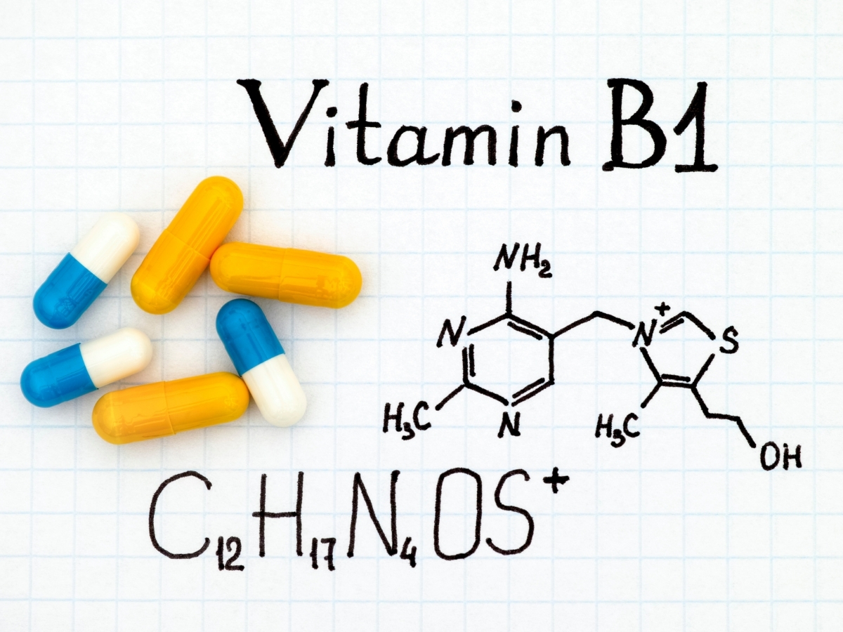 B1-vitamin képlete és kémiai vegyjele négyzetrácsos lap háttéren, sárga és kék-fehér kapszulák