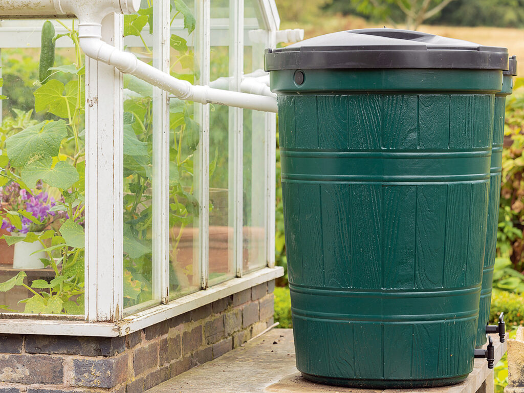 Two green water butts outside a greenhouse being used for water - Nők Lapja