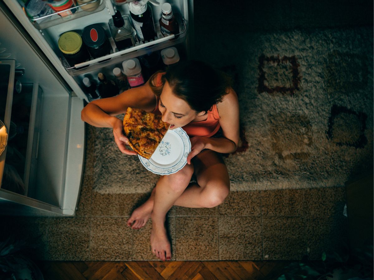 fiatal nő késő este pizzát eszik a hűtőszekrény előtt